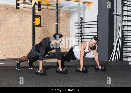 Smiling man training with dumbbells near arabian friend in sports center Stock Photo