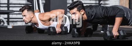 Arabian man working out with dumbbells near sportsman in gym, banner Stock Photo