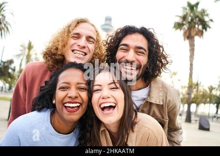 Group of four multi-ethnic young friends having fun. Smiling cheerful people looking at the camera outdoors. Stock Photo