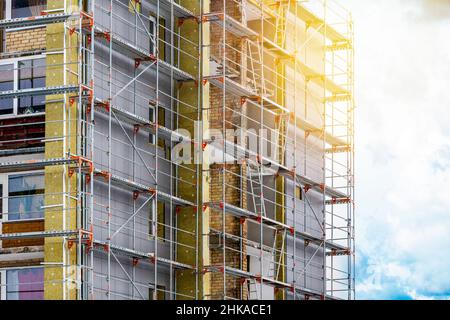 Scaffolding on multistory building facade during renovation. Exterior passive house wall heat insulation with mineral wool. Insulation facade of multi Stock Photo