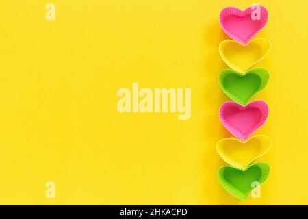 Colored silicone heart shaped molds dish for baking cupcakes lined in rowright side on yellow paper background. Template for lettering, text or your d Stock Photo