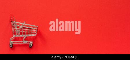 Small empty shopping trolley cart on red background. Concept sale. Top view Copy space. Stock Photo