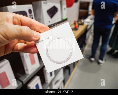 Paris, France - Sep 24, 2021: POV male hand holding new Apple Computers MagSafe magnetic charger with customers defocused in background - accessory to charge wirelessly the iphone Stock Photo