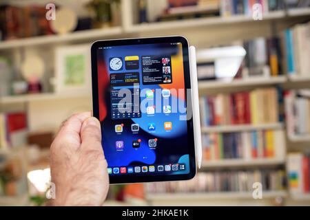 Paris, France - Oct 25, 2021 POV male hand holding new latest ipad Mini Pro professional by Apple computers against bookshelves background Stock Photo