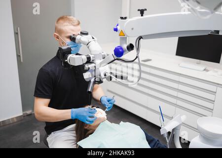 Professional young male dentist uses a microscope to treat a female patient. Modern technologies in dentistry Stock Photo