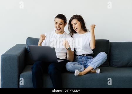 Overjoyed excited millennial couple getting good news, celebrating success, goal achieving, winning prize. Happy man and woman sitting on couch with l Stock Photo