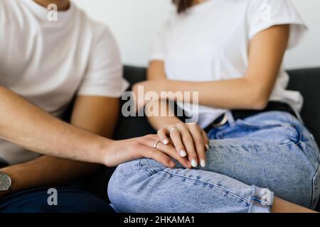 Close up woman and man in love sitting on couch two people holding hands. Symbol sign sincere feelings, compassion, loved one, say sorry. Stock Photo