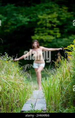 Young woman balancing on narrow wooden walkway, arms outstretched to help balance Stock Photo