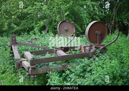 Abandoned farm tilling machinery left to rust in a field and now overgrown with weeds Stock Photo