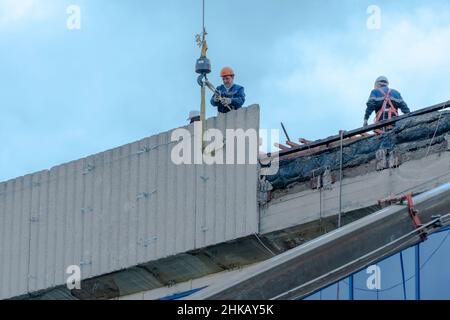 Moscow,Russia,05,10,2021:Restoration,reconstruction and repair of the building.Construction workers in hard hats install concrete slabs on the roof of Stock Photo