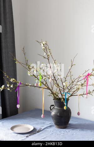 Blooming cherry branches decorated with colorful ribbons with Easter eggs, Happy Easter, table setting Stock Photo