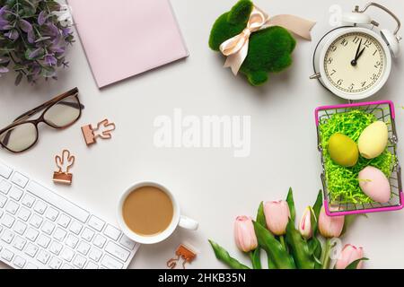 Top view of the desktop. Cup of coffee glasses keyboard alarm clock flowers with easter decorations. Flat lay copy space Stock Photo