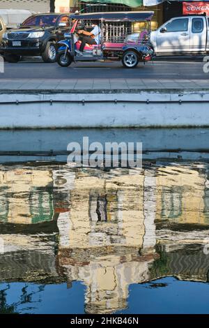 Reflections of an old European-style building in Klong (canal) Lod alongside Atsadang Rd in Bangkok, Thailand, a tuk-tuk on the street above Stock Photo