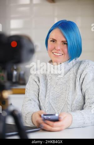 Happy video blogger woman talking on camera. Cheerful white female with dyed blue hair speaking on live stream Stock Photo