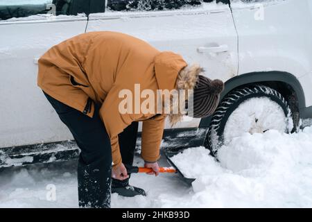 A man digs out a stalled car in the snow with a car shovel. Transport in winter got stuck in a snowdrift after a snowfall, sat on the bottom. First ai Stock Photo