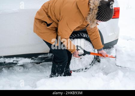 A man digs out a stalled car in the snow with a car shovel. Transport in winter got stuck in a snowdrift after a snowfall, sat on the bottom. First ai Stock Photo