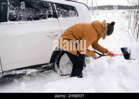 A man digs out a stalled car in the snow with a car shovel. Transport in winter got stuck in a snowdrift after a snowfall, sat on the bottom. First ai Stock Photo