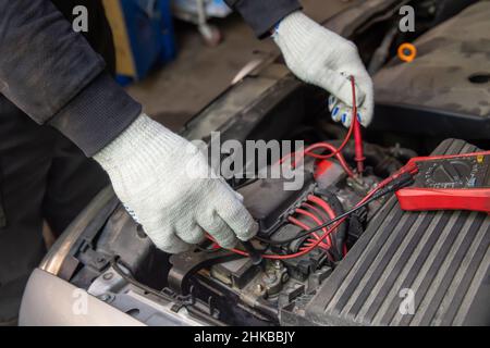 Selective focus an auto mechanic uses a multimeter voltmeter to check the voltage level in a car battery. Maintenance and repair. Stock Photo