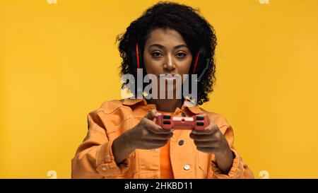 KYIV, UKRAINE - JANUARY 26, 2022: curly african american woman holding blurred joystick isolated on yellow Stock Photo