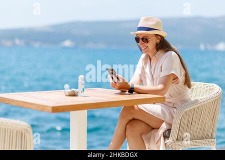 Young lady in dress sitting at the table in cafe near the sea Stock Photo