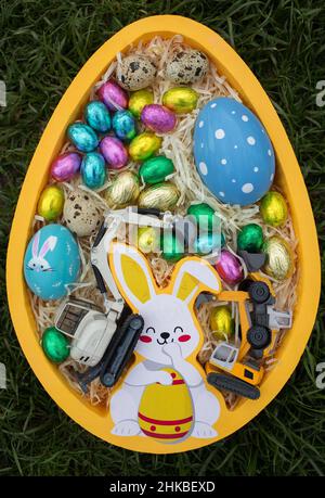 Symbolic Easter gift for construction companies. A collection of various colored and chocolate Easter eggs and two models of an excavator in a box in Stock Photo