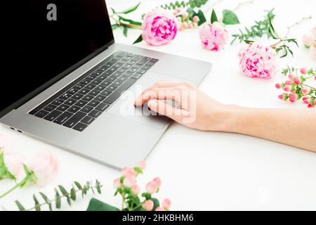 Woman using laptop. Workspace with female hands, laptop and pink flowers on white. Stock Photo