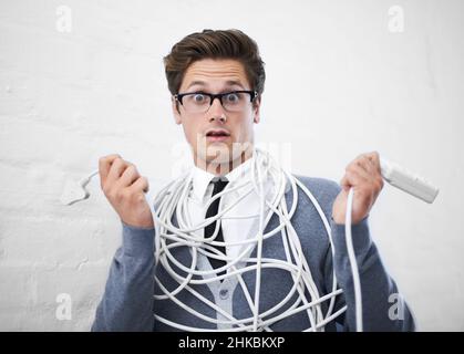 Lost in wires. A young nerdy guy tangled up in cables. Stock Photo