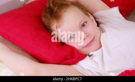 Morning in bed kids. Cute funny cheerful little boy wakes up and lies in bed in the morning, stretches and smiles. 4k video clip. Relaxation in bed. Stock Photo