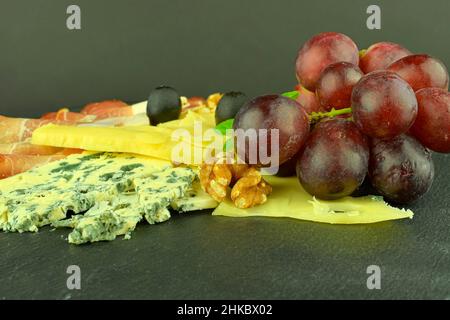 Tray with Schwarzwald ham, cheeses, walnuts, black olives. Decorated with basil. Food on slate backgroud. Copy space Stock Photo