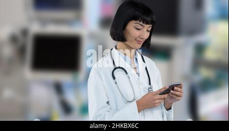 Smiling asian young female doctor using smart phone while standing in hospital Stock Photo