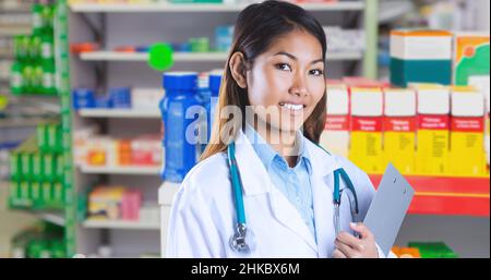 Smiling asian young female doctor holding clipboard while standing in hospital chemist Stock Photo