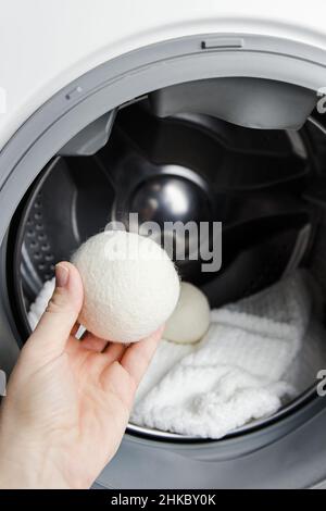 Woman using wool dryer balls for more soft clothes while tumble drying in washing machine concept. Discharge static electricity and shorten drying. Stock Photo