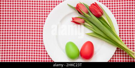 Easter Holiday table. Egg red and green and tulips decoration on white plate, checkered tablecloth background, top view, Stock Photo
