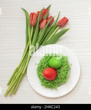 Easter table celebration. Egg nest and red tulips decoration on white wooden background, top view, Spring Holiday Stock Photo