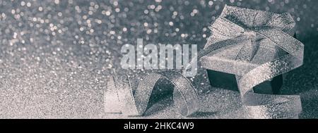 Christmas gray silver background - gift box with shiny bow on an abstract background with festive glitter and bokeh. Banner, panorama with free space Stock Photo