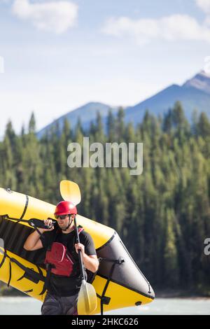 Scenic image of man carrying yellow raft (packraft) in wilderness. Stock Photo