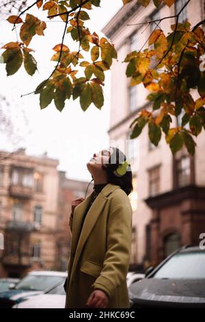 Young woman listening music in headphones standing on street in autumn Stock Photo