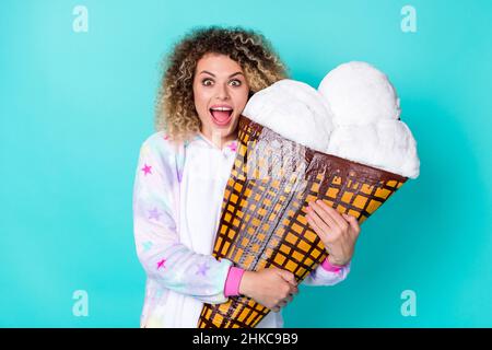 Photo of impressed millennial curly hairdo lady hug ice-cream wear kigurumi isolated on blue background Stock Photo