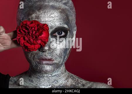 Portrait of a Beautiful young woman with a clay mask on her face, which is covered with silver paint Stock Photo