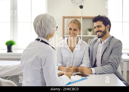 Happy young married couple in hospital consults with experienced doctor about planning pregnancy. Stock Photo
