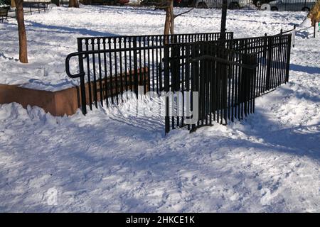 A black fence on the white snow in a park during a sunny winter day Stock Photo