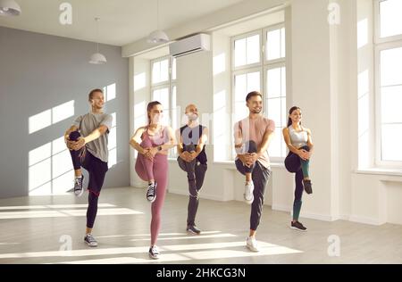 Young energetic people during group sports training doing high knee exercise in bright gym. Stock Photo