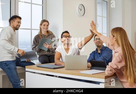 Cheerful multiracial students give each other five as they prepare for exam or lesson. Stock Photo