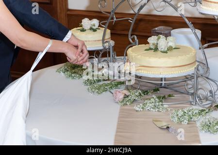 Hands of the newly married bride and groom cut a slice of the wedding cake together holding the knife. Stock Photo