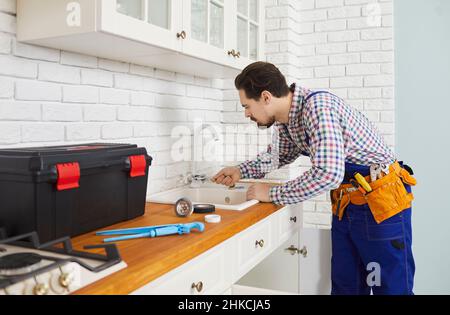 Professional plumber installs or repairs faucet and sink in kitchen of apartment. Stock Photo