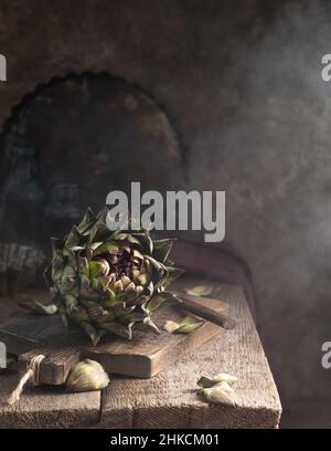 Fresh green artichoke on rustic wooden background with napkins and soft light, close up Stock Photo