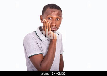 frustrated and unhappy young man having a puzzled expression, holding his hand on his cheek. Stock Photo