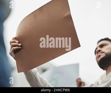 Make them hear you. Low angle shot of a handsome young man holding a sign while taking part in a political rally. Stock Photo