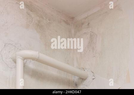 Repair of the joint of the two white dirty walls corner at the ceiling, construction work with old pipe heat home heating water. Stock Photo