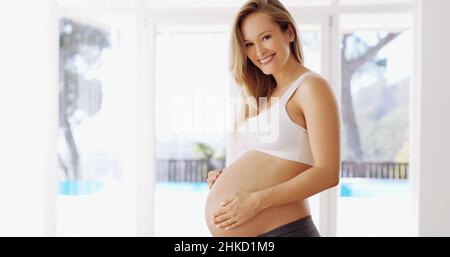 The little one comes first. Cropped portrait of an attractive young pregnant woman rubbing her baby bump. Stock Photo